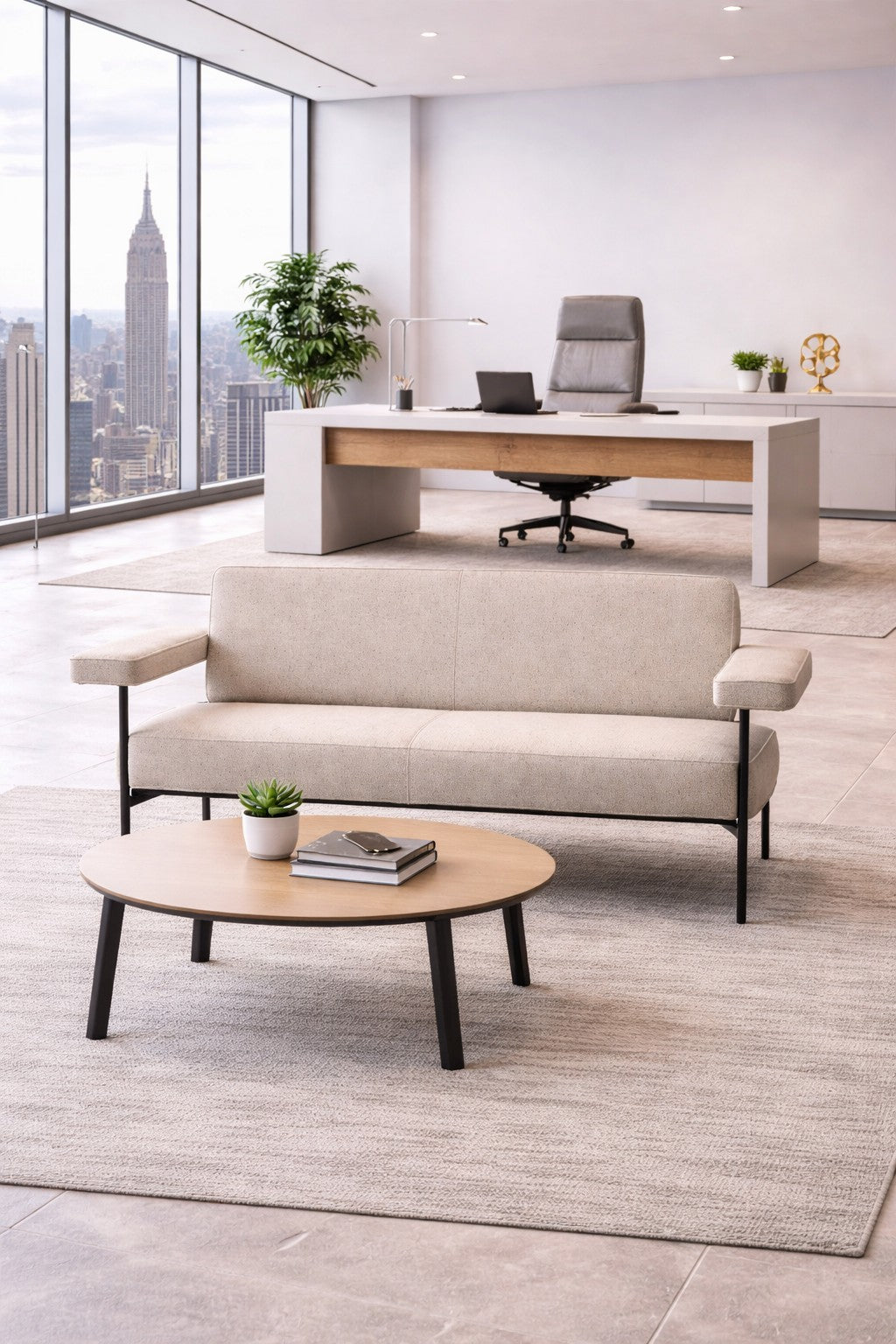 Un bureau moderne avec un canapé Monsieur Bureau Canapé d'accueil Tilos - 2 personnes en beige, une table basse ronde, des plantes en pot, et un bureau avec ordinateur portable et chaise près de grandes fenêtres donnant sur l'Empire State Building.