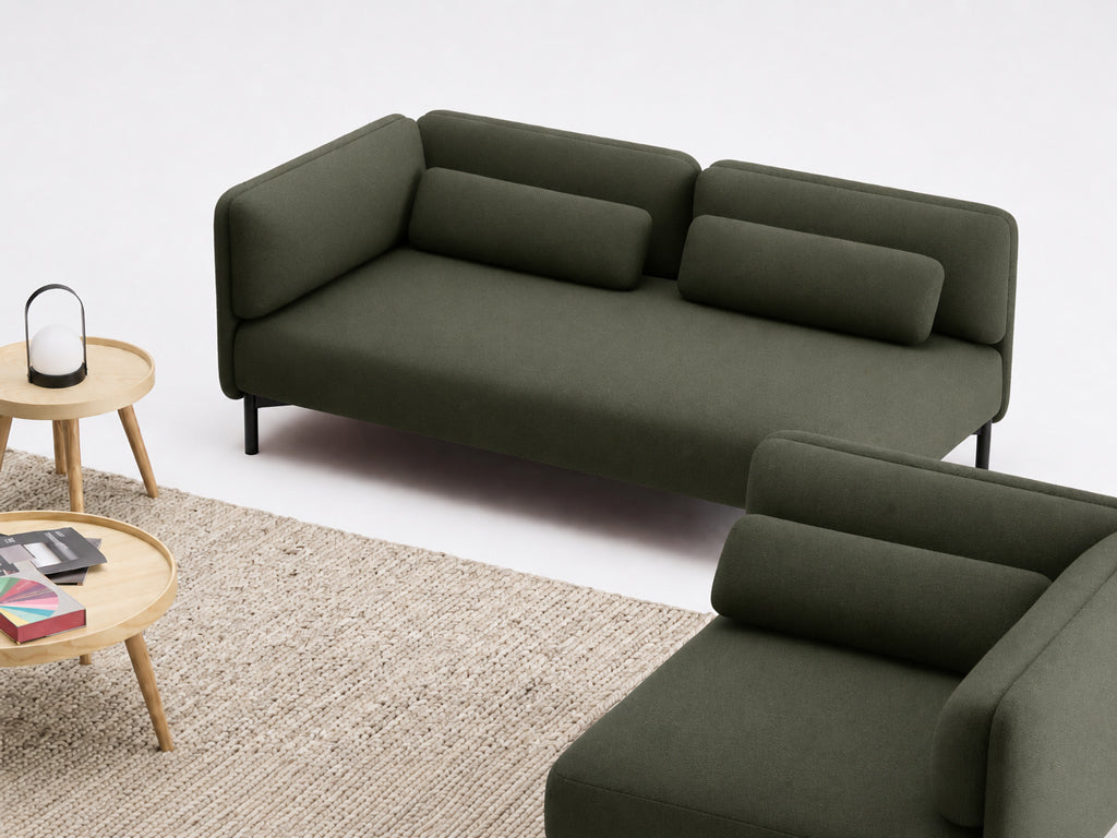 Un salon moderne présente le Canapé d'accueil modulaire Aurea - 1 accoudoir de Monsieur Bureau en vert foncé, associé à un tapis beige texturé et à une table basse en bois clair avec des livres et une lanterne, le tout sur fond blanc.