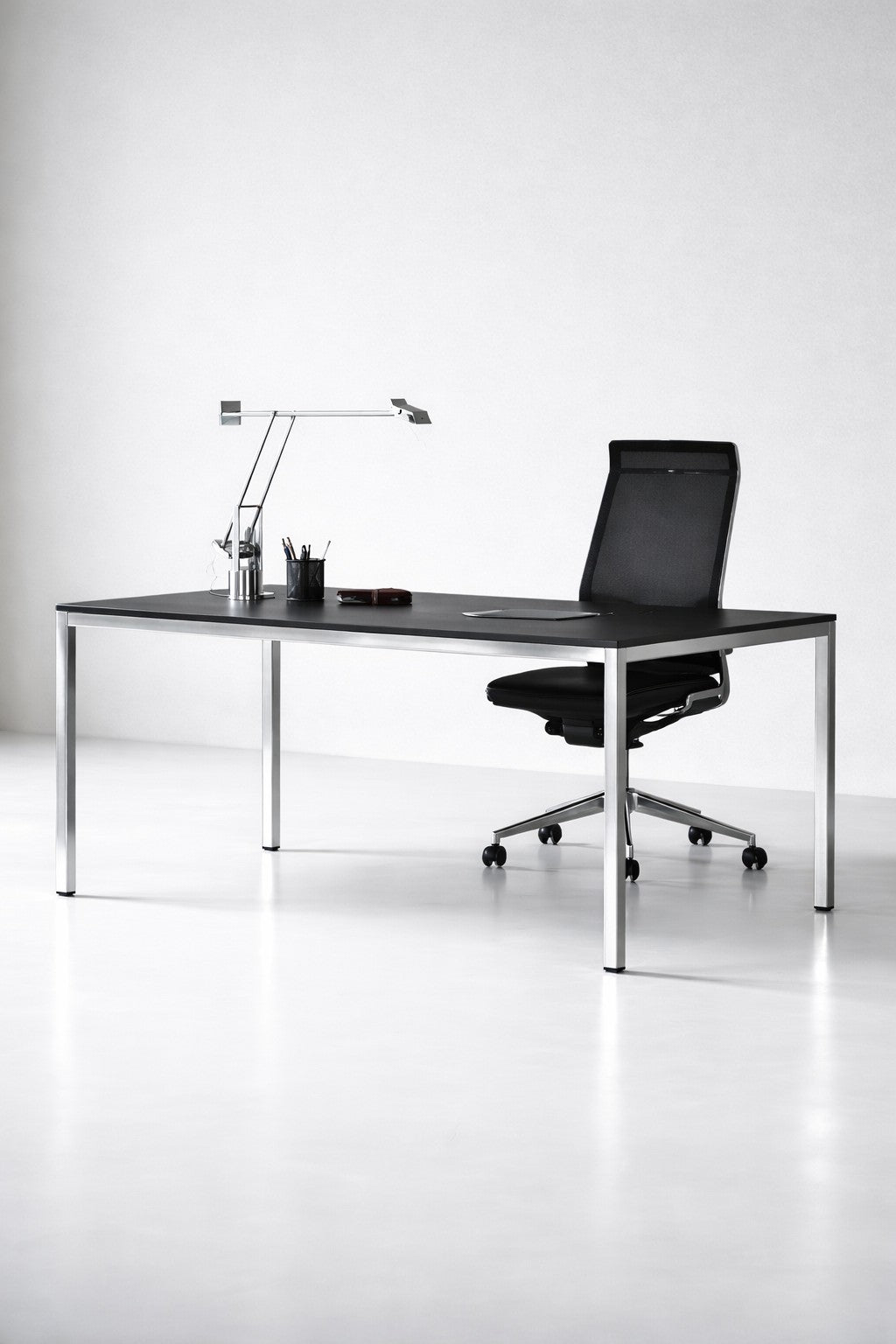 Un espace de travail minimaliste avec le Bureau de direction Nova L200 x P100 cm de Monsieur Bureau, associé à une chaise moderne en maille, une lampe de bureau et des fournitures de bureau, le tout sur un fond blanc épuré.