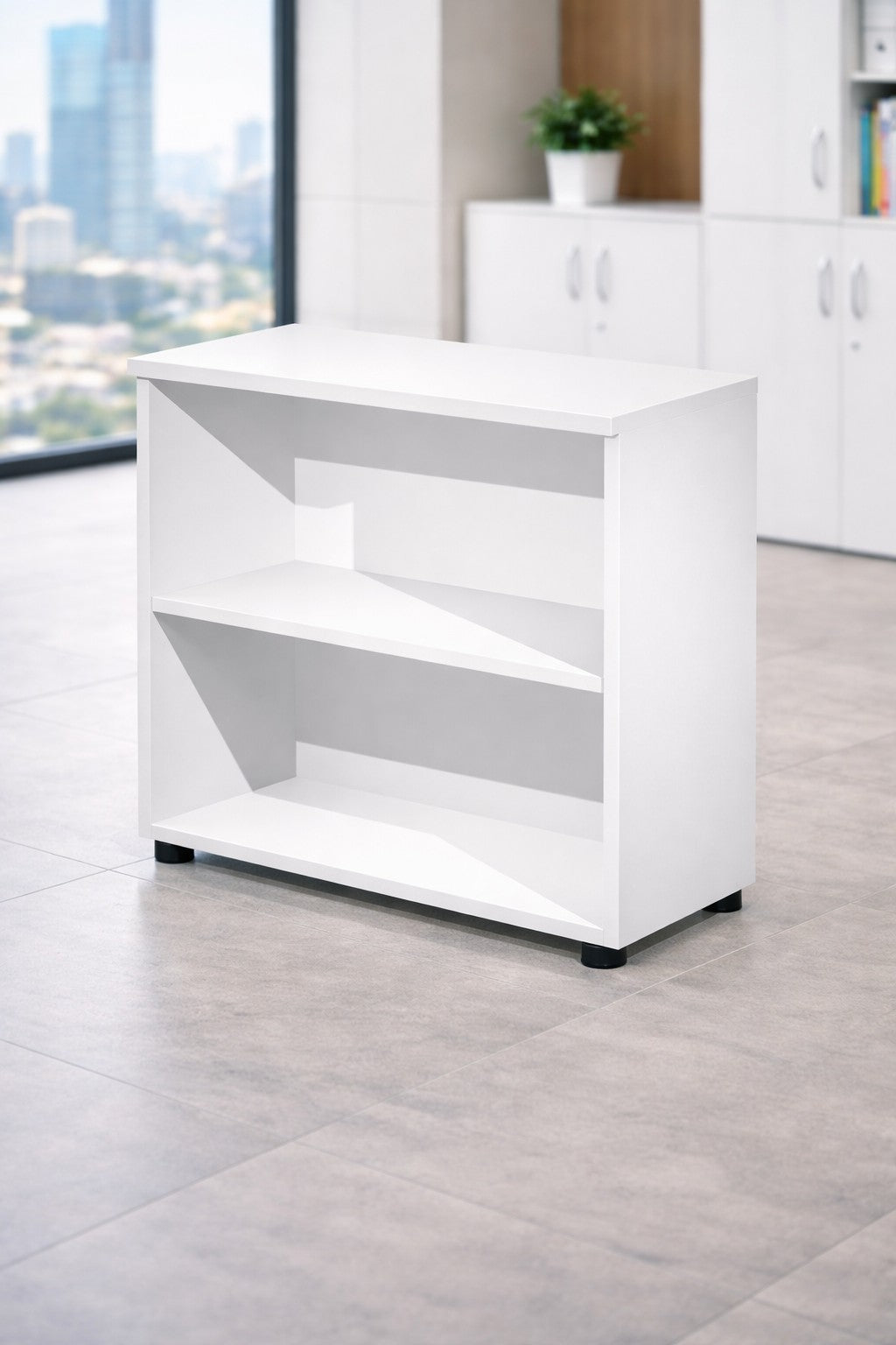 Une "Armoire ouverte basse de bureau H72 Effect & Budget" blanche de Monsieur Bureau est posée sur un sol carrelé dans un bureau moderne avec de grandes fenêtres, des armoires blanches et une petite plante en pot, offrant un rangement professionnel optimal.#finitions_blanc