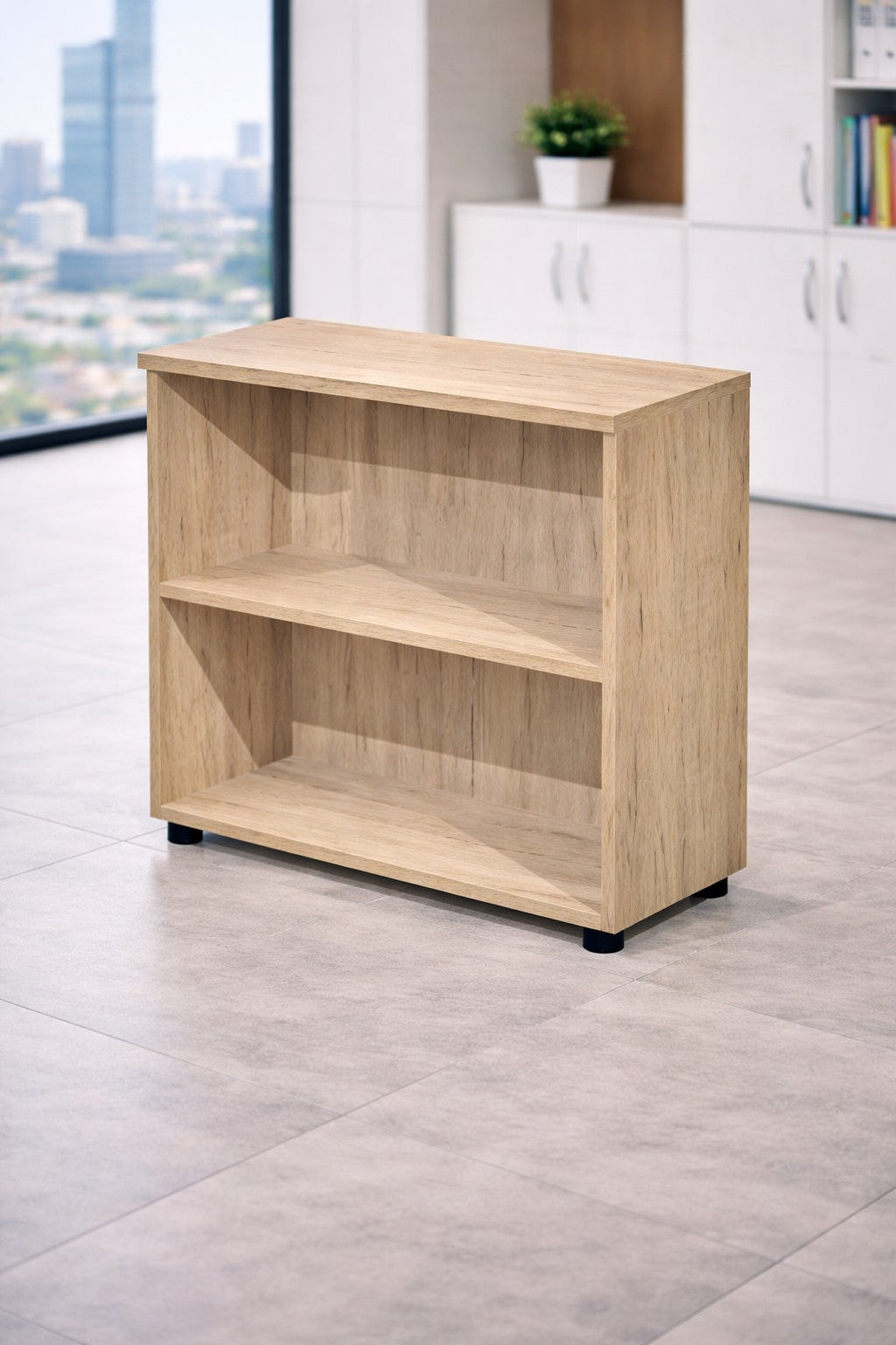 L'Armoire ouverte basse de bureau H72 Effect & Budget de Monsieur Bureau, une armoire compacte en bois clair avec deux étagères, est posée sur un sol carrelé dans un bureau moderne avec des armoires blanches, une plante et de grandes fenêtres avec vue sur la ville - idéal pour le rangement professionnel.#finitions_chene_canadien