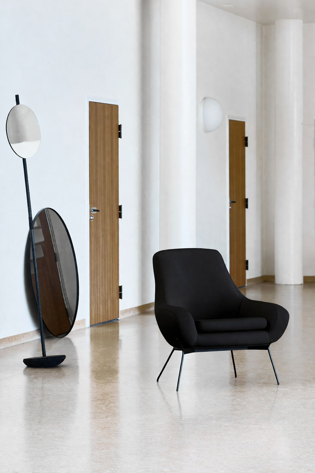 Le Fauteuil Lounge Nomi de Susanne GRØNLUND pour Monsieur Bureau est posé sur un sol clair et poli, près d'un miroir circulaire sur pied, encadré par des portes en bois fermées et des murs blancs, créant une atmosphère contemporaine raffinée.#finitions_anthracite