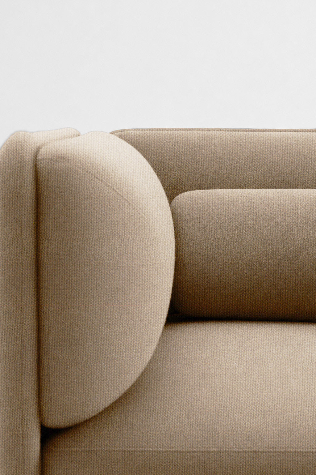 Gros plan sur un canapé beige moderne avec un accoudoir arrondi et un coussin cylindrique, sur un fond clair - idéal pour être associé au Monsieur Bureau Fauteuil d'accueil modulaire Aurea.