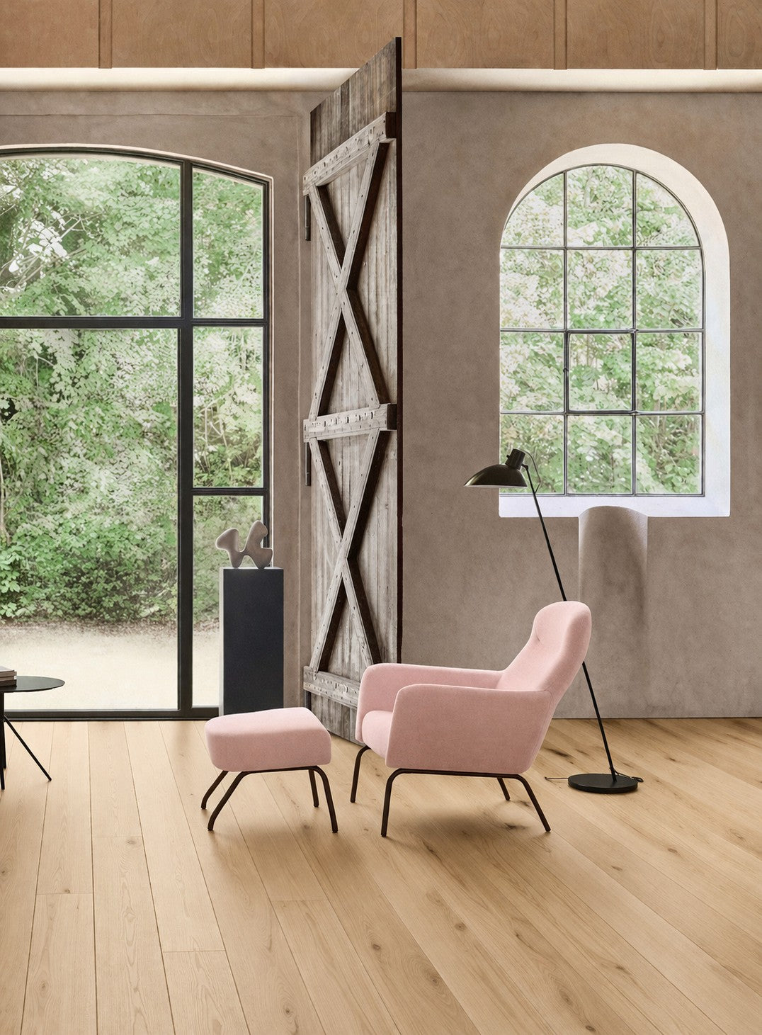 Une pièce moderne avec de grandes fenêtres cintrées, des planchers en bois clair et le Fauteuil lounge Fjord bas dossier de Busk+Hertzog pour Monsieur Bureau - une chaise rose avec ottoman - associée à un lampadaire noir et aux arbres verts à l'extérieur.
