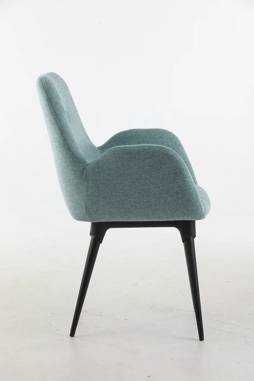 Le Fauteuil d'accueil et réunion Shino de Monsieur Bureau se caractérise par un revêtement bleu-vert clair, un dossier incurvé avec accoudoirs et quatre pieds élancés en métal noir. Il est présenté en vue latérale sur un fond blanc uni.