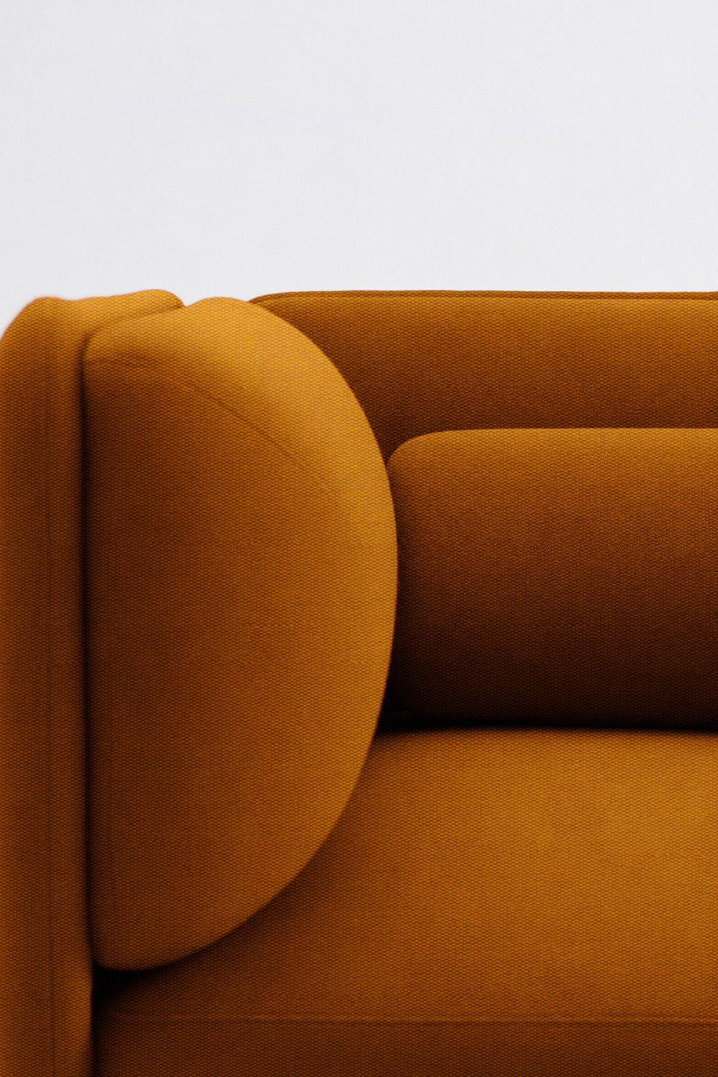Gros plan sur le Fauteuil d'accueil modulaire Aurea de Monsieur Bureau, revêtu d'un tissu jaune moutarde, mettant en valeur l'accoudoir, le dossier partiel et le coussin cylindrique sur un fond blanc uni.