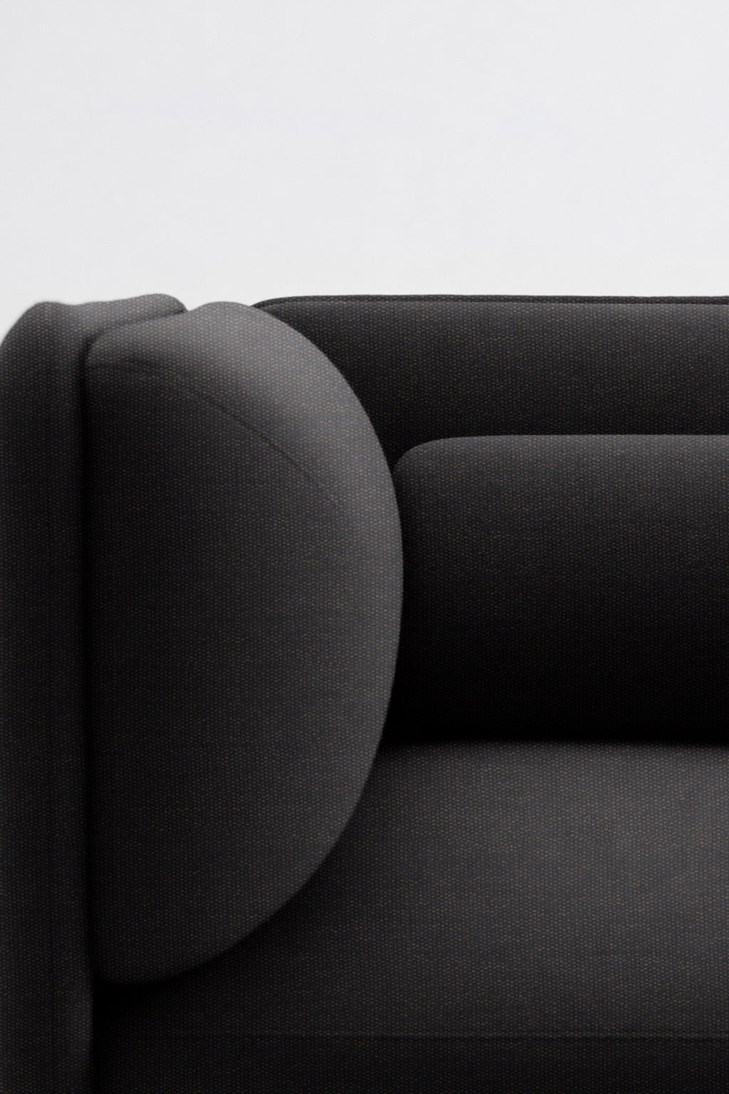 Gros plan sur un canapé moderne noir aux accoudoirs arrondis et au revêtement lisse et minimaliste, qui complète parfaitement le style épuré du Fauteuil d'accueil modulaire Aurea de Monsieur Bureau, sur un fond blanc uni.