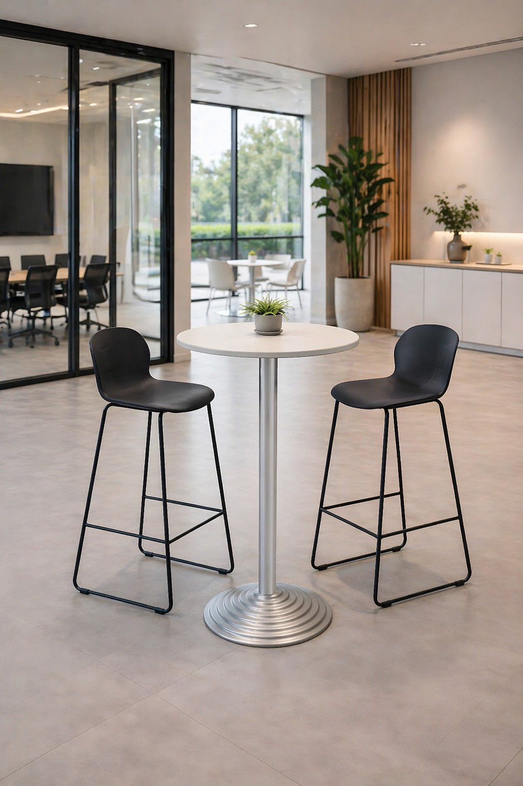 Un salon de bureau moderne présente une table ronde blanche Monsieur Bureau Guéridon haut 6000 - Pied en Fonte, deux tabourets de bar noirs, une petite plante en pot sur la table, de grandes fenêtres, une salle de réunion vitrée et des plantes d'intérieur en arrière-plan.