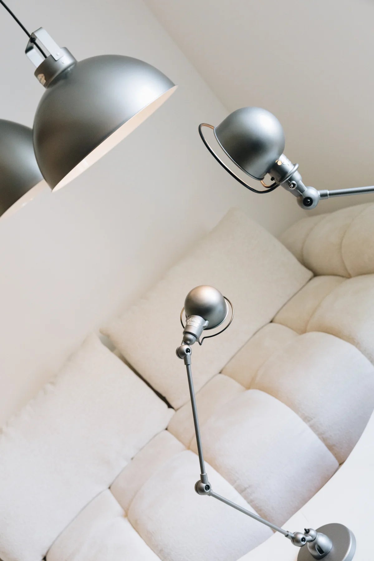 Gros plan sur la Lampe de bureau articulée design Signal de Monsieur Bureau, dotée d'accoudoirs réglables, exposée au-dessus et à côté d'un canapé blanc capitonné contre un mur blanc uni dans un salon minimaliste.