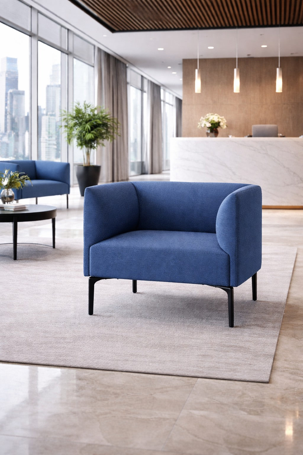 Un salon moderne présente le Fauteuil d'accueil Kay de Monsieur Bureau en bleu sur un tapis beige, des sols en marbre, une table basse ronde avec des fleurs, de grandes fenêtres et un bureau de réception professionnel en marbre à l'arrière-plan.#combo_bleu_marine_noir