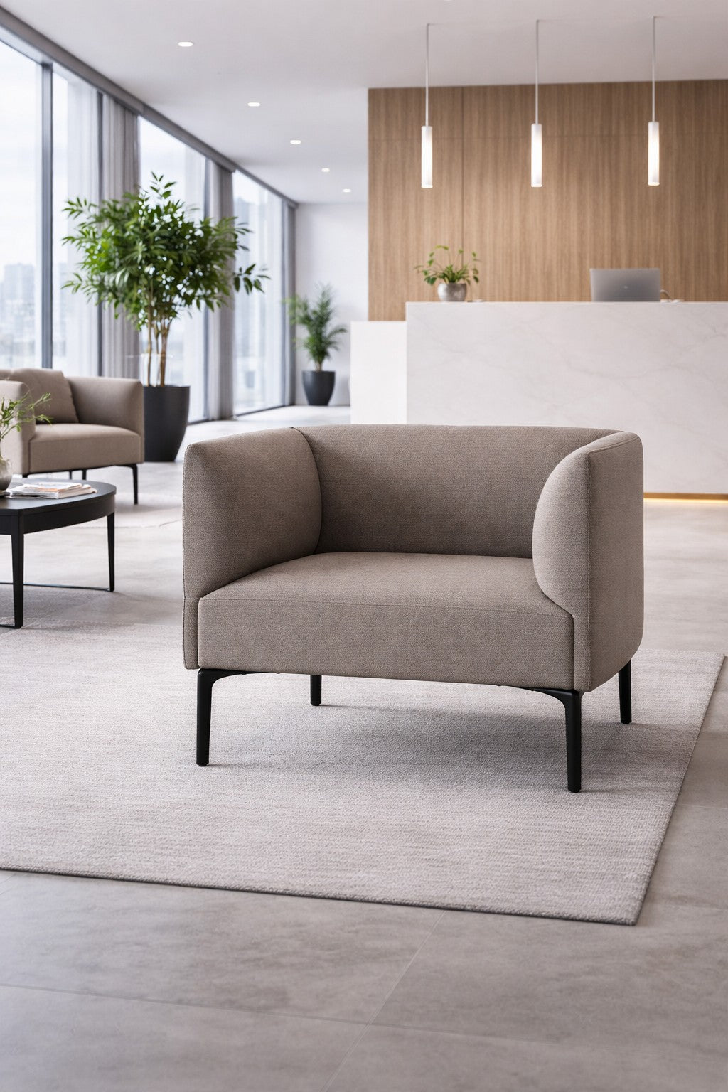Le hall d'entrée d'un bureau moderne présente la chaise de réception Kay de Monsieur Bureau en beige sur un tapis clair, une table basse ronde, des plantes en pot, de grandes fenêtres et un bureau de réception blanc avec des lampes suspendues en arrière-plan.