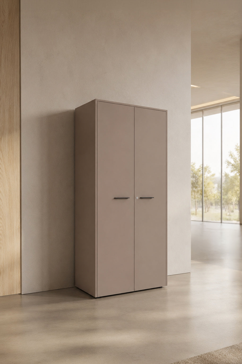 L'Armoire haute Passe Partout 2 portes de Monsieur Bureau, dans une finition minimaliste taupe avec des poignées élégantes, se trouve contre un mur clair dans une pièce moderne et spacieuse avec de grandes fenêtres et des vues sur les arbres à l'extérieur.#finitions_taupe