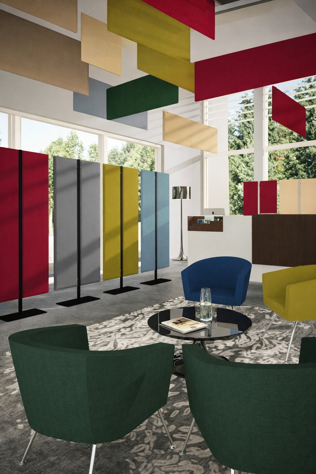 Un salon moderne avec des fauteuils colorés, une table basse ronde en verre et des panneaux Monsieur Bureau Cloison acoustique Aria H140/H160/H180 en rouge, jaune, beige et bleu, placés devant de grandes fenêtres donnant sur des arbres verts.