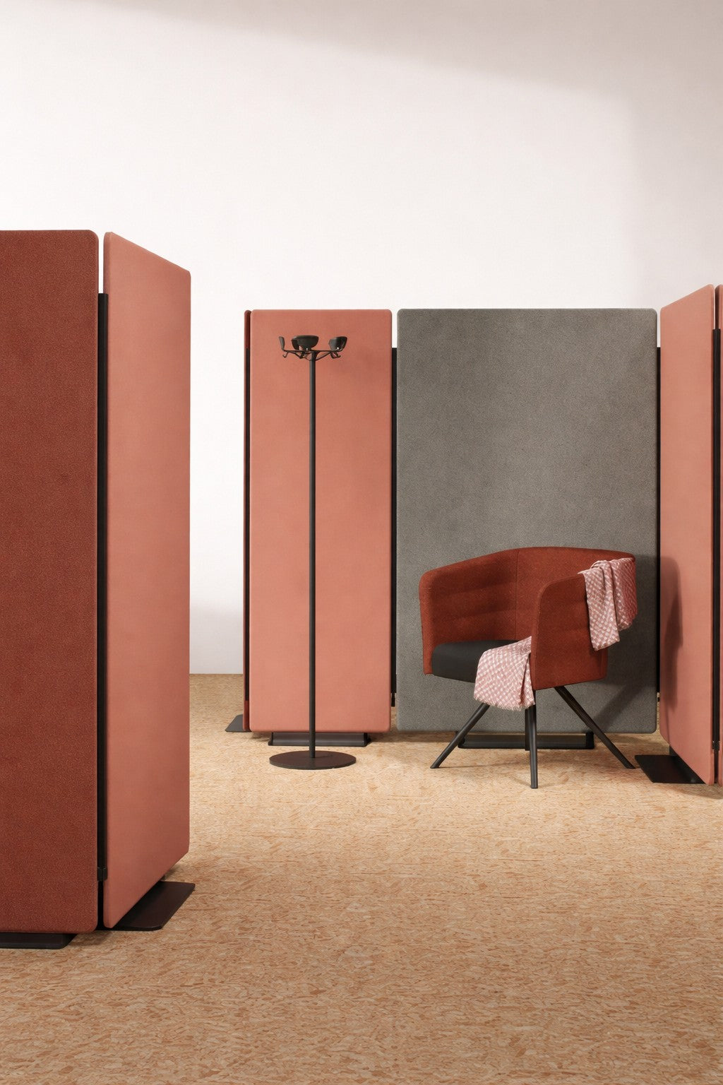 Un bureau ouvert moderne présente de grands panneaux Cloison Acoustique Silenza H160 avec Zip de Monsieur Bureau en rouille, un panneau gris, une chaise pivotante rouille texturée drapée d'un tissu rouge-blanc, et un porte-manteau noir sur une moquette beige.