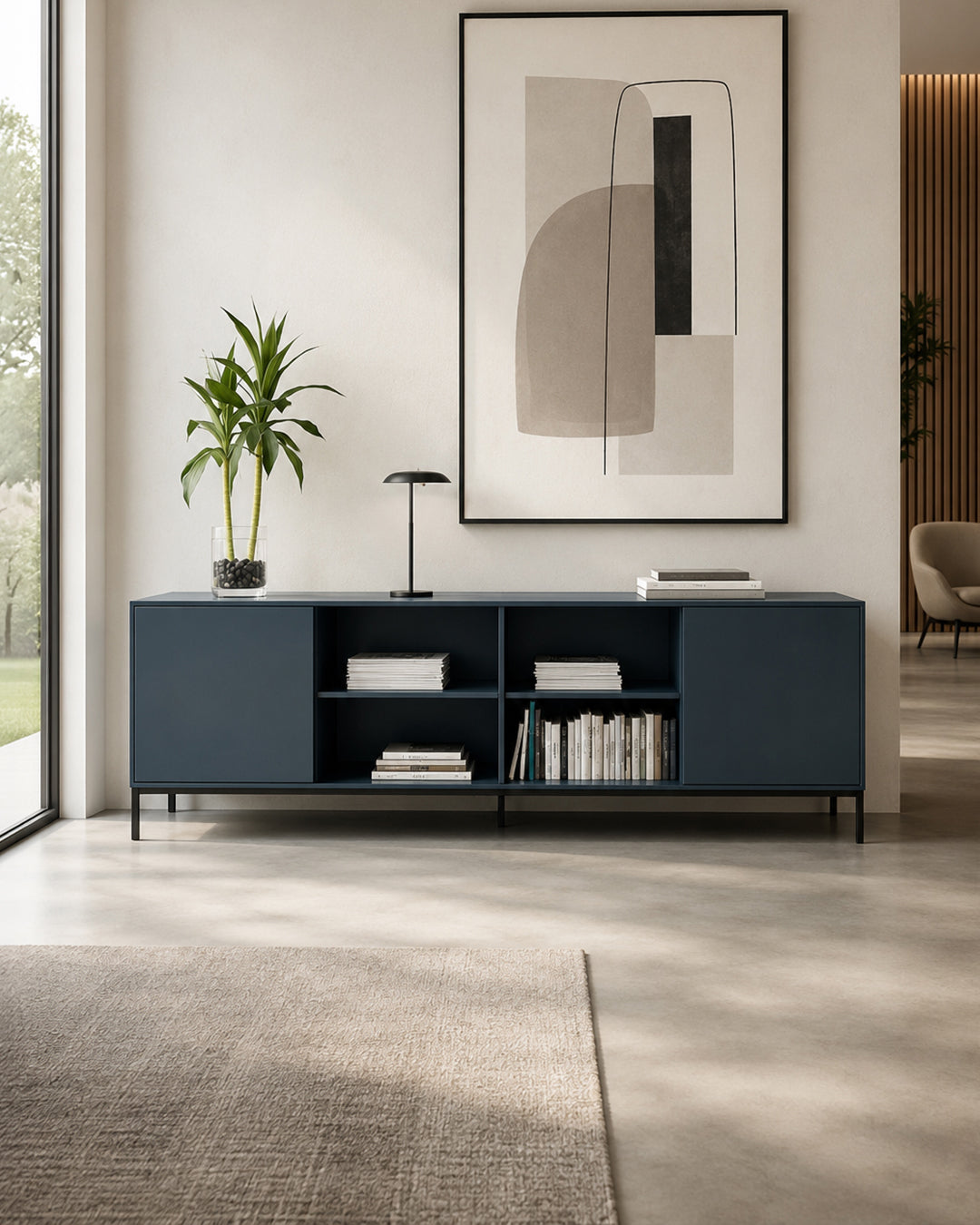 Le Buffet Quadra - 2 portes et 4 niches de Monsieur Bureau en bleu présente des livres, de la décoration et une plante. Un tableau abstrait représentant une silhouette de femme est suspendu au-dessus, tandis qu'une applique murale minimaliste sur la gauche rehausse l'ambiance moderne d'inspiration italienne.#finitions_bleunuit