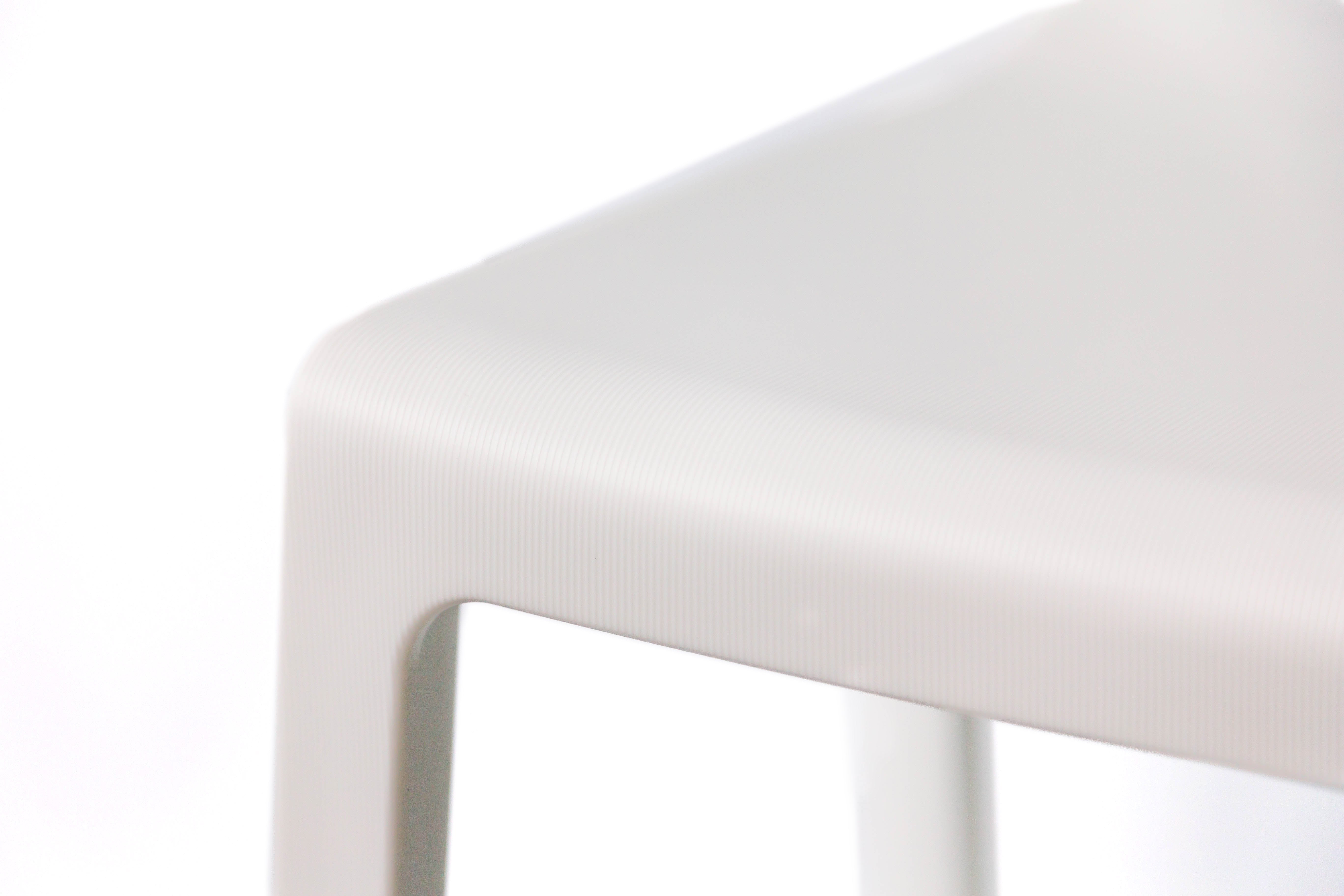 Gros plan sur l'angle d'une chaise Monsieur Bureau Chaise Extérieur Indi Bellini Empilable, une chaise monobloc moderne en polypropylène gris clair ou blanc aux bords lisses et arrondis, présentée sur un fond blanc.
