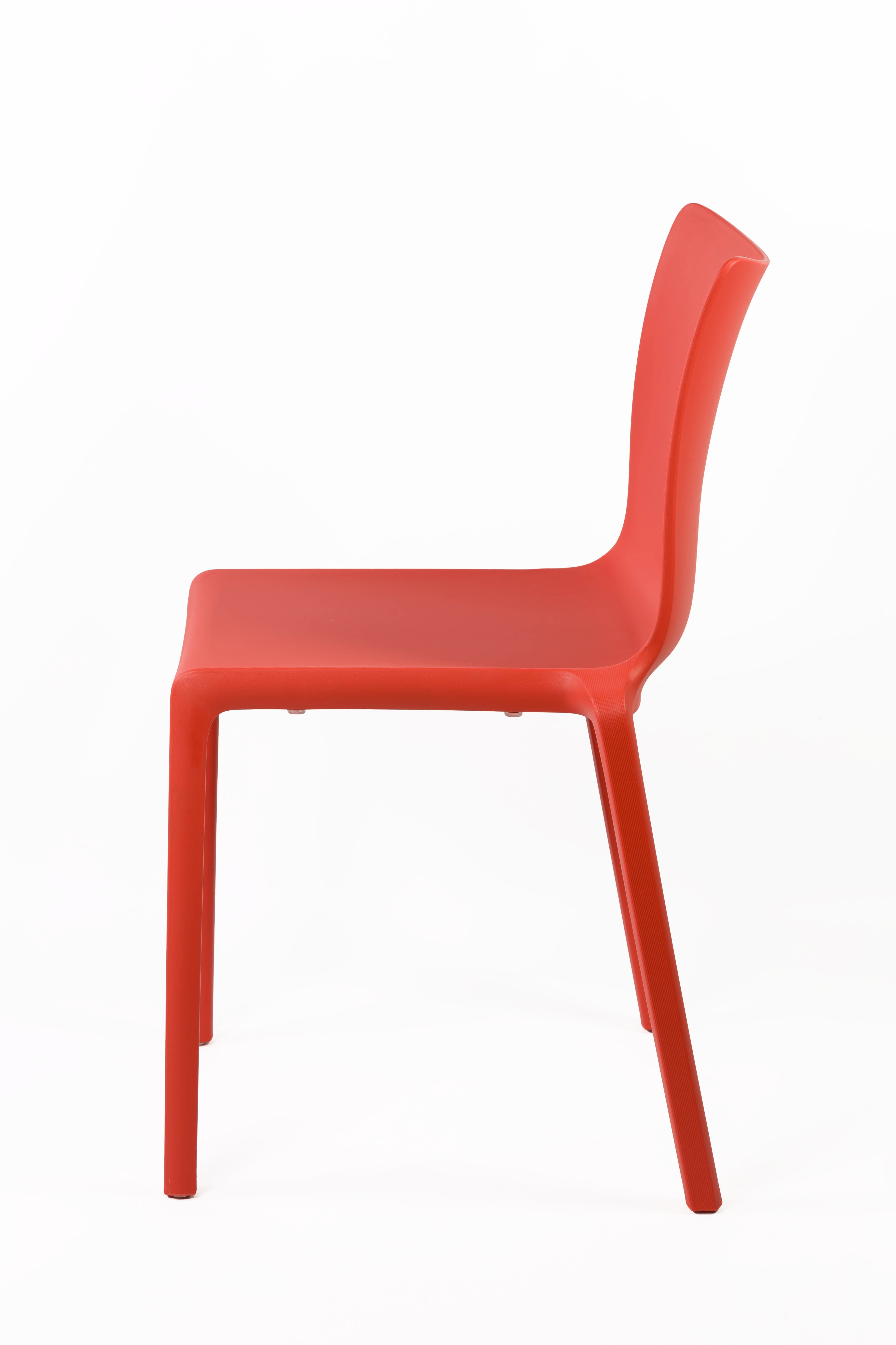 La Chaise Extérieur Indi Bellini Empilable de Monsieur Bureau est une chaise monobloc moderne et minimaliste en polypropylène rouge avec un dossier lisse et incurvé et quatre pieds droits, présentée de profil sur un fond blanc uni.