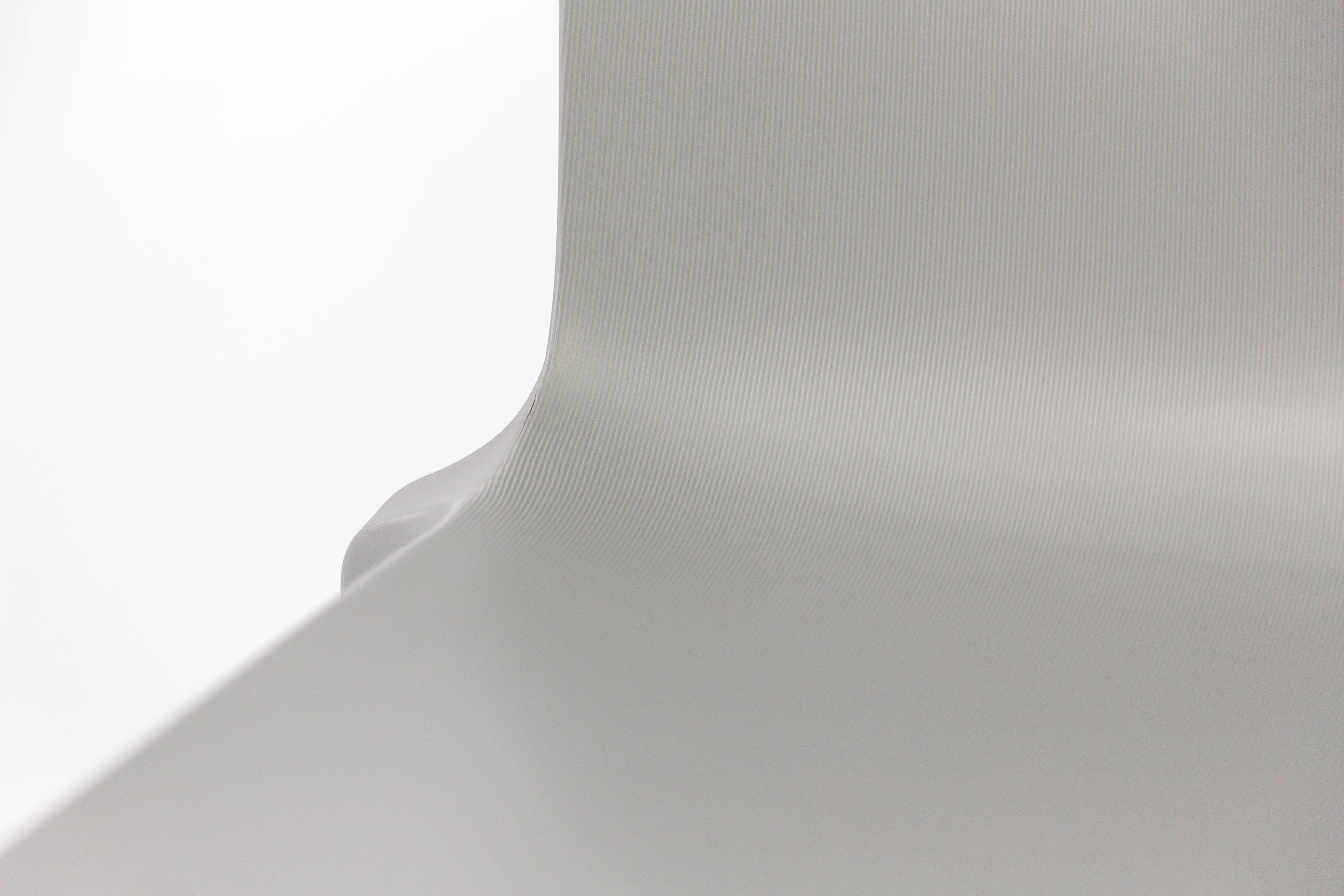 Gros plan sur la surface lisse et monobloc en polypropylène gris clair de la Chaise Extérieur Indi Bellini Empilable de Monsieur Bureau, aux lignes horizontales subtiles, sur un fond blanc uni, dans un style minimaliste.