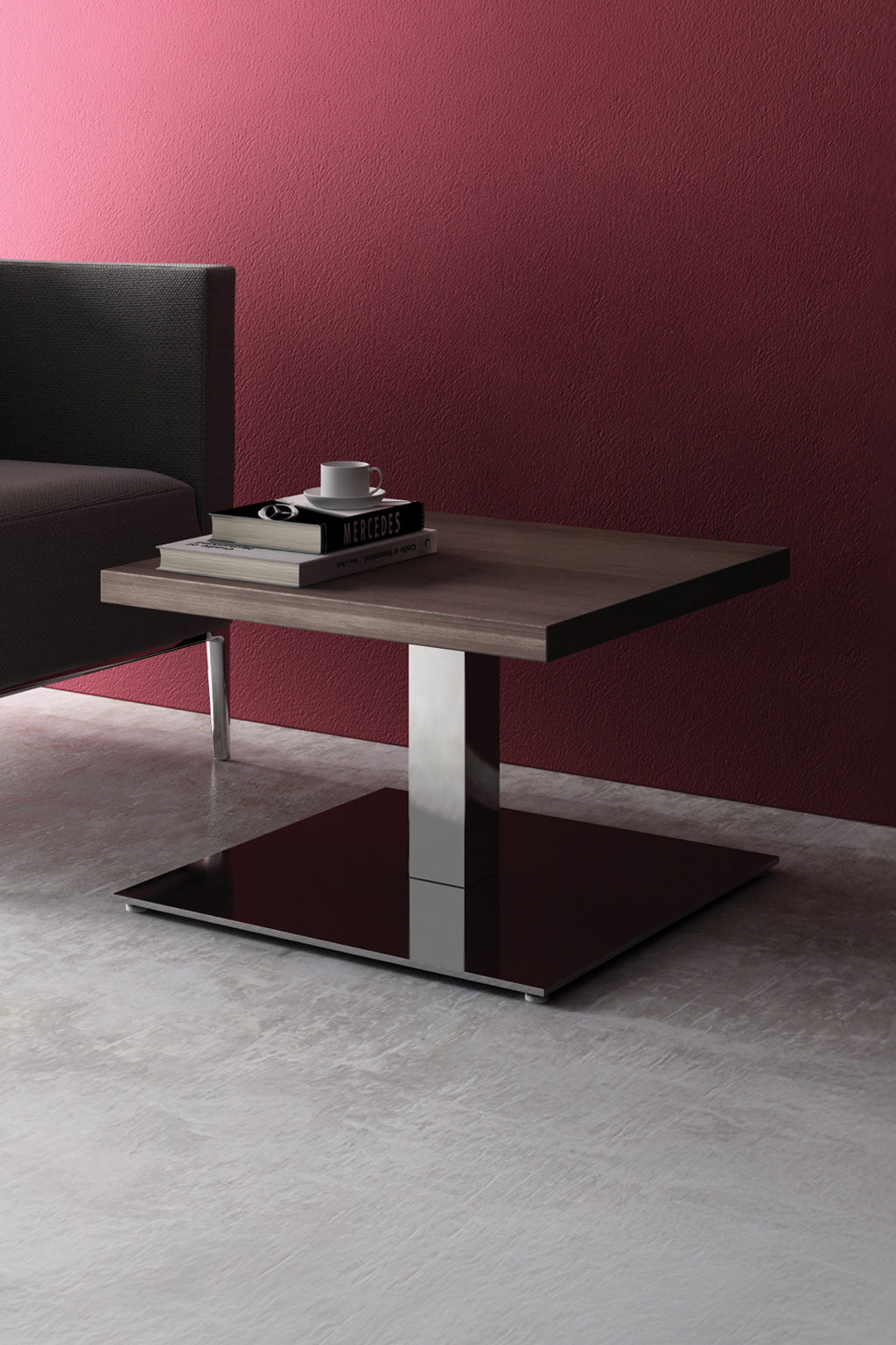 La Table basse Coffee Pop - H40 cm de Monsieur Bureau, composée d'un plateau carré en bois et d'une base en métal de fabrication italienne, présente une tasse et un livre sur un sol en béton à côté d'un canapé sombre placé contre un mur rouge.