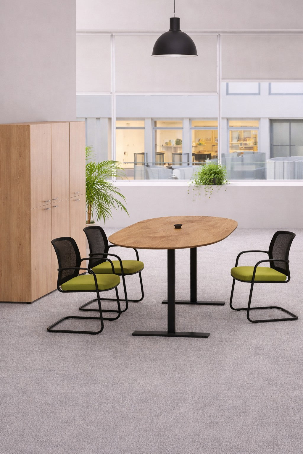 Bureau moderne avec un Monsieur Bureau Table tonneau électrique Top & Down - 6/8 personnes, trois chaises noires avec coussins verts, un meuble en bois, des plantes en pot, de grandes fenêtres et une lampe suspendue noire - idéal mobilier de réunion.