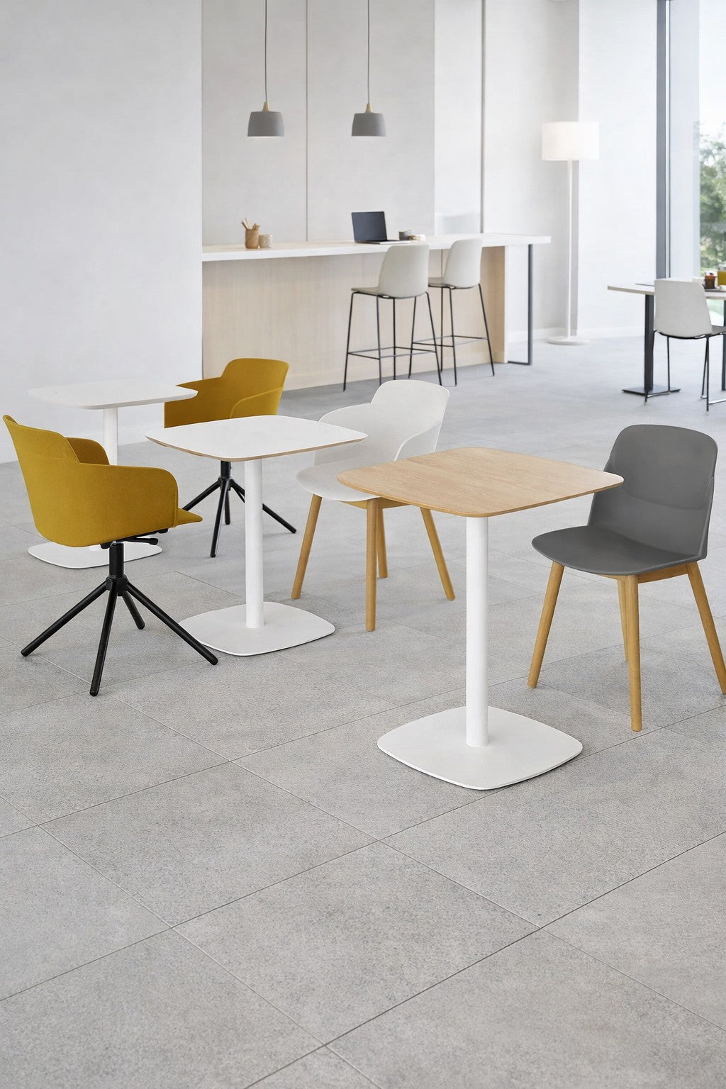 Un café moderne et minimaliste avec des sols carrelés de couleur claire et des tables blanches Monsieur Bureau Table de collectivité Kafeta (MDF), ainsi que des chaises jaunes, grises et blanches. Un comptoir à hauteur de bar au fond est équipé de tabourets, d'ordinateurs portables et de lampes suspendues.