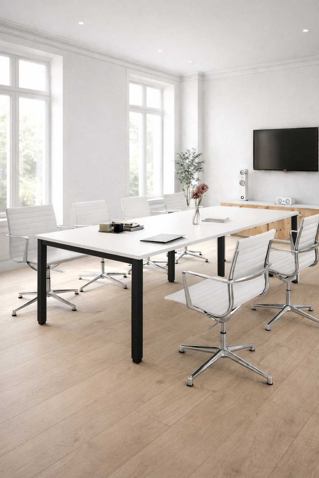 Une salle de conférence moderne dotée d'une table de réunion rectangulaire 6 à 14 personnes Tempo de Monsieur Bureau, de huit chaises pivotantes blanches, d'un téléviseur mural, de fenêtres allant du sol au plafond, d'un parquet en bois clair et d'un vase avec des fleurs sur un buffet.#combo_blanc_noir