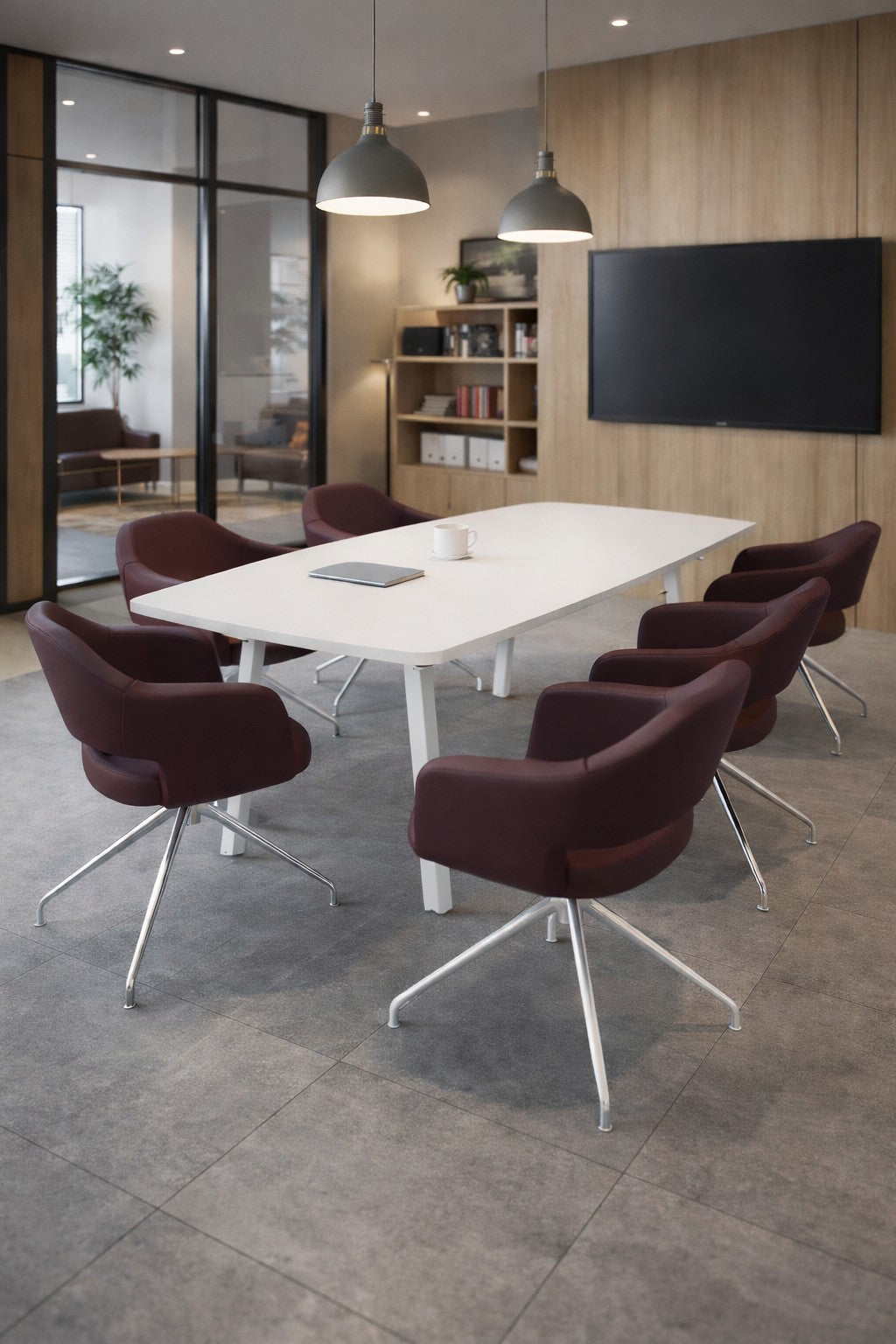 Une salle de conférence moderne avec Monsieur Bureau Table de réunion tonneau ATMOSPHERIC pour 6 personnes, six chaises marron, une télévision murale, des lampes suspendues, des étagères en bois et des murs en verre donnant sur un autre bureau avec une plante.