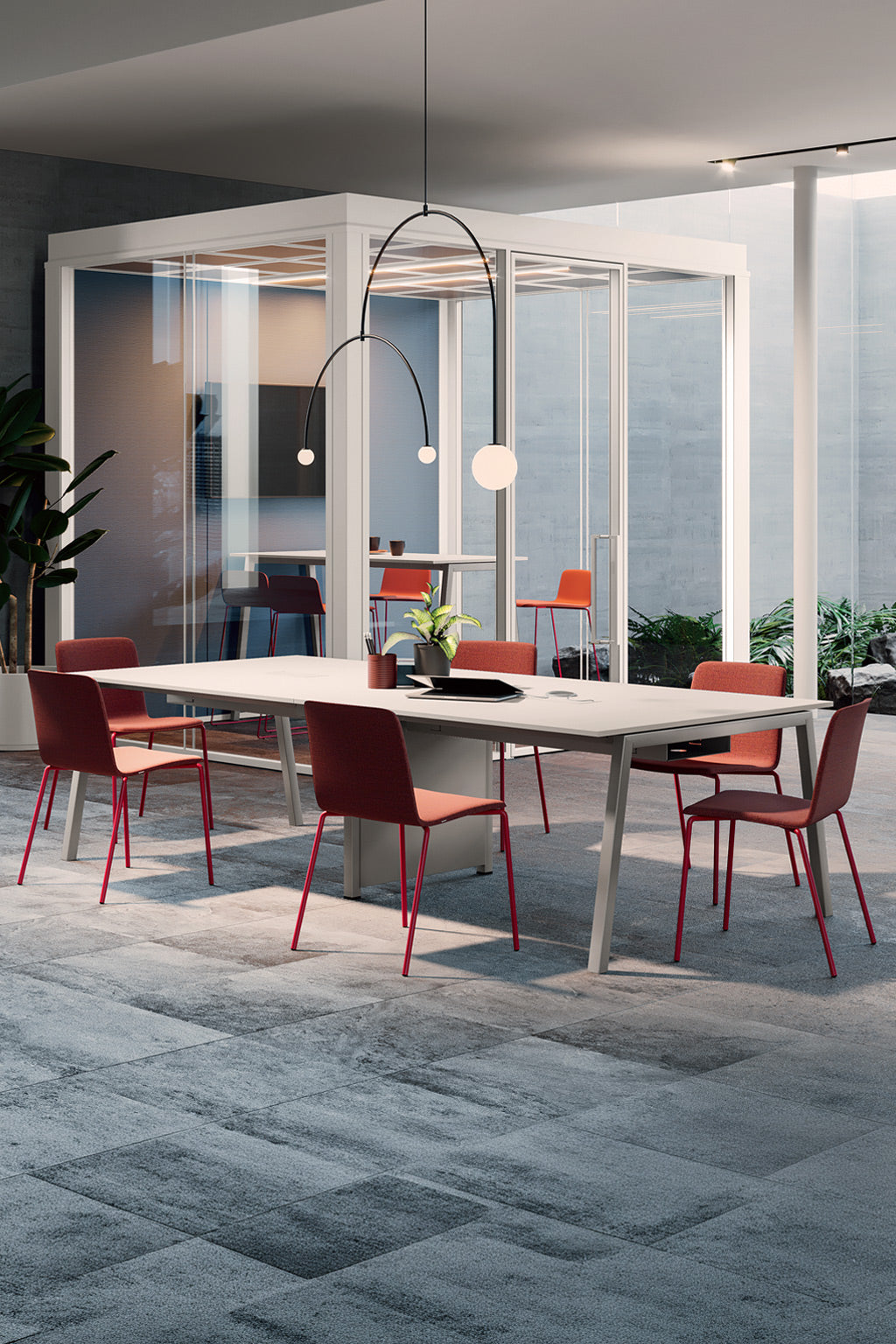Bureau moderne avec une table de réunion Pop Ace P125 / P165 - Pieds métal inclinés par Monsieur Bureau, des chaises rouges, une suspension noire minimaliste et une plante en pot. Une nacelle en verre et d'autres chaises rouges mettent en valeur un aménagement tertiaire élégant à la lumière naturelle.